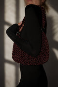 Handcrafted rhinestone cord macrame bag in a deep Red Wine burgundy shade held by a model in a black outfit.