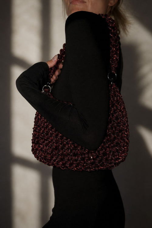 Handcrafted rhinestone cord macrame bag in a deep Red Wine burgundy shade held by a model in a black outfit.